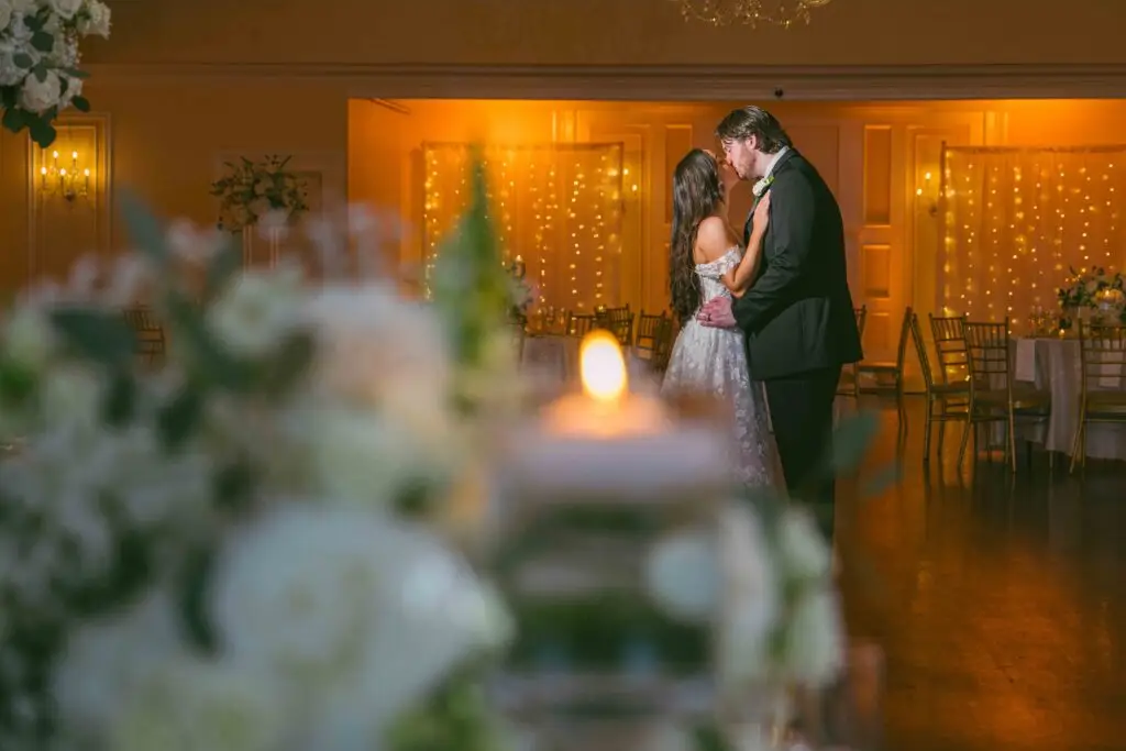 Bride and groom share a kiss in the center of their ballroom wedding reception, surrounded by elegant decor and guests.