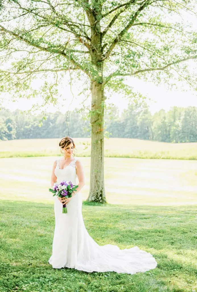 Sunlit bride standing under a willow tree with dappled light