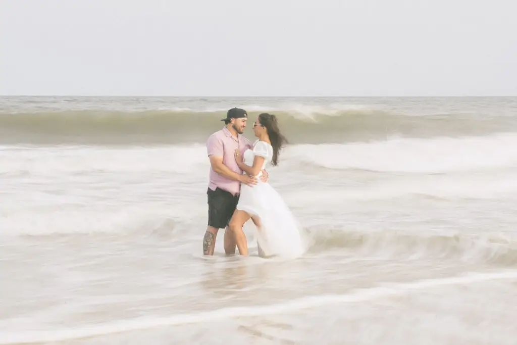Romantic Long Island beach engagement photo of couple embracing in ocean waves at sunset by JS Visions Photography