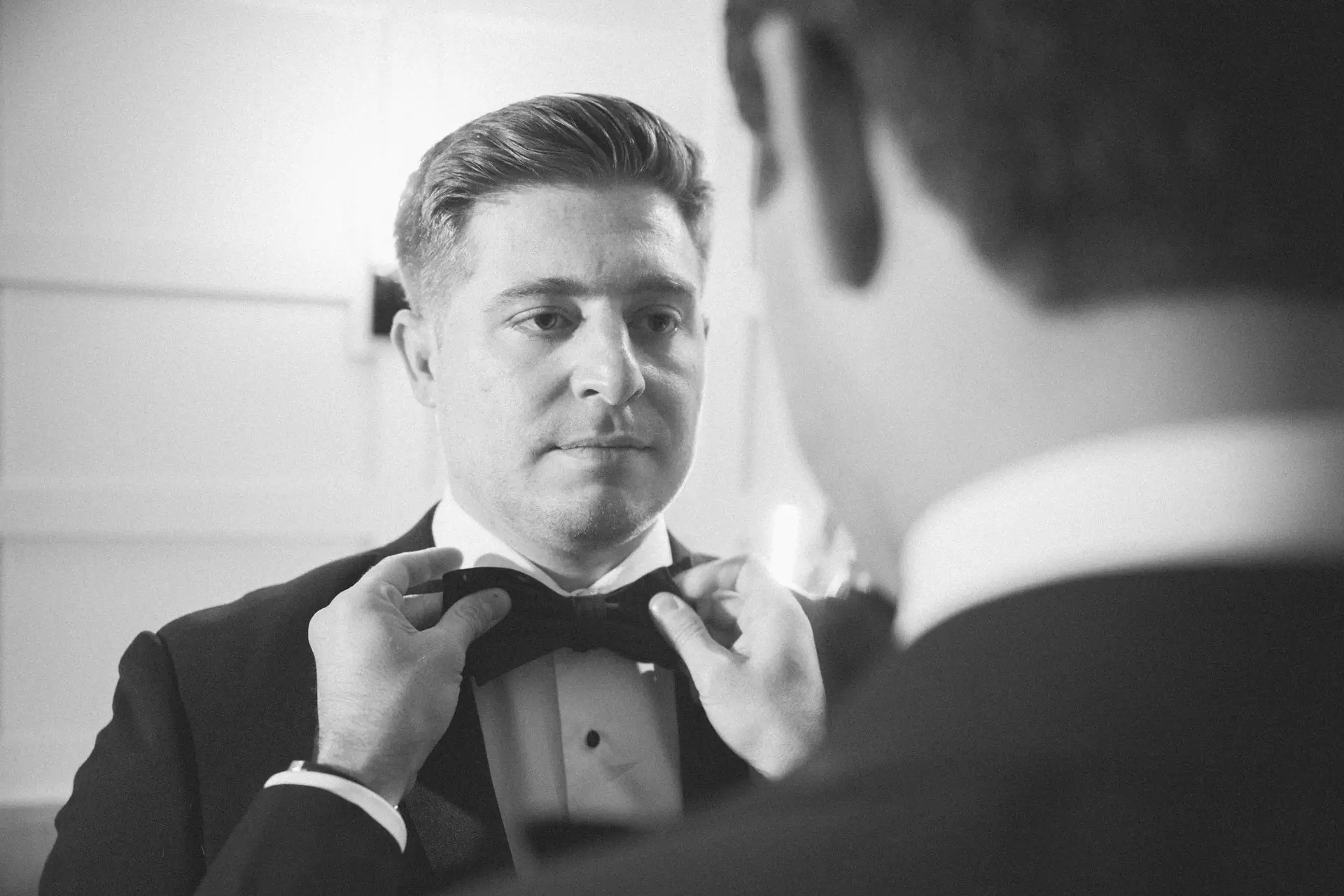 Best man adjusting the groom's black bow tie before a wedding ceremony in New York City