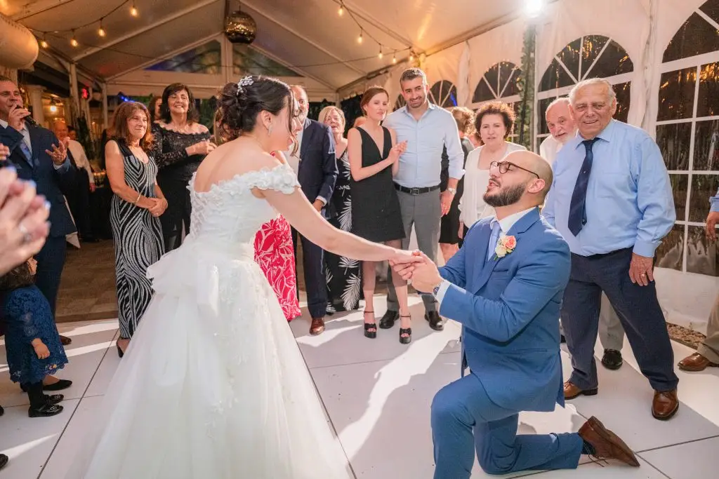 Groom on bended knee holding bride's hand during first dance at Rare650, Syosset, NY​