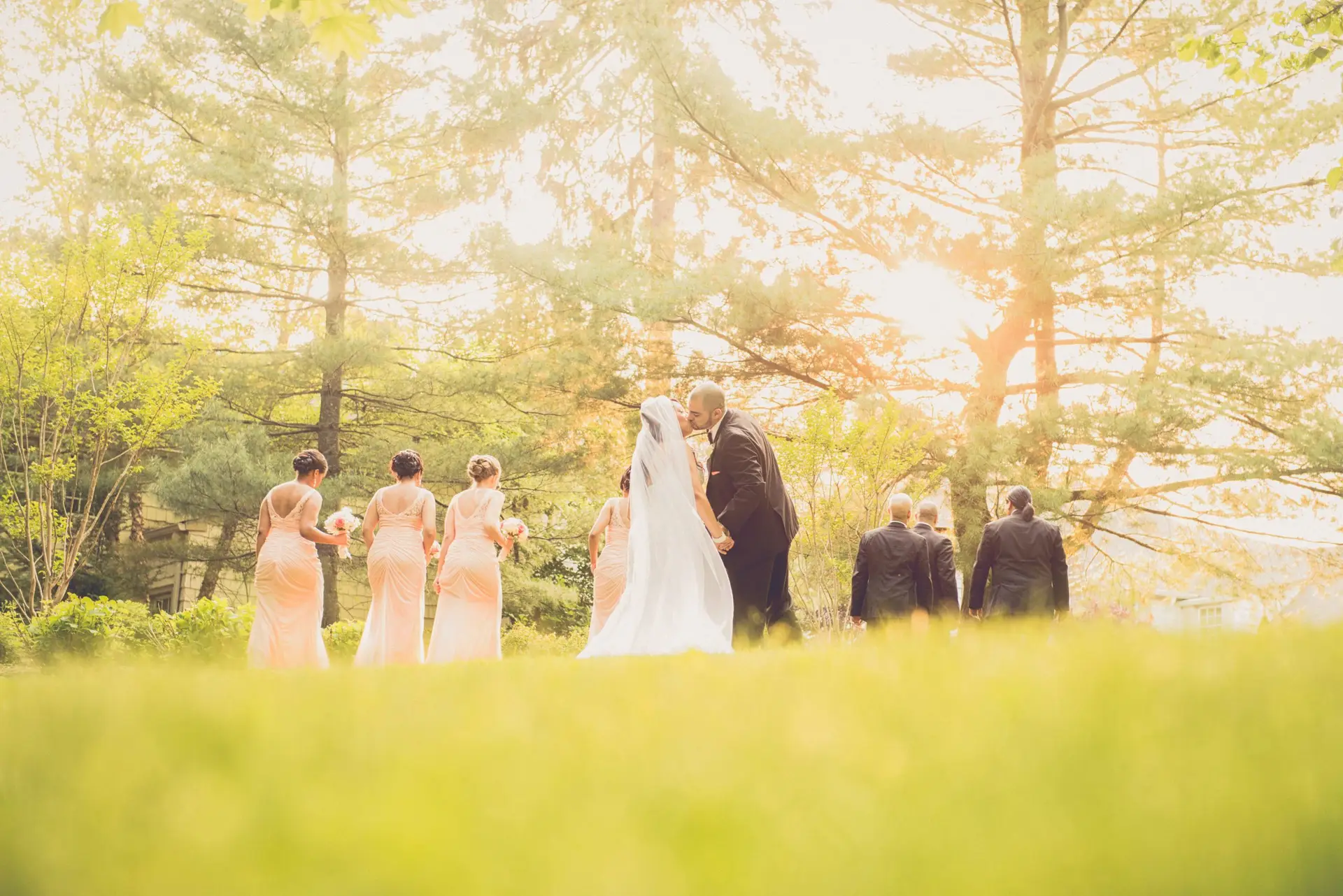 Bride and groom kiss while bridal party walks ahead