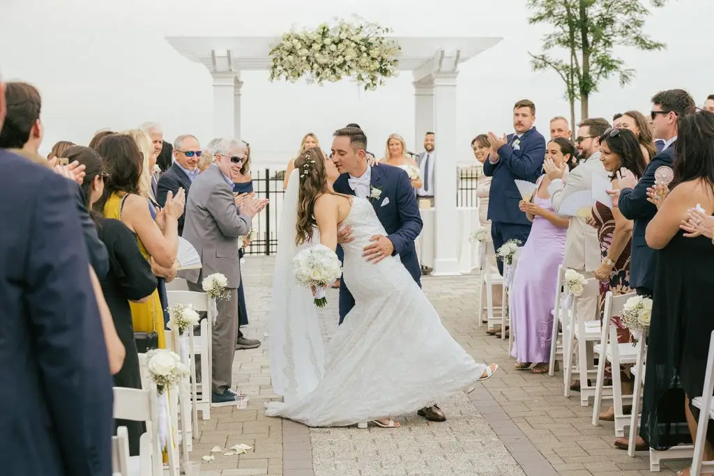 Bride and groom share a romantic kiss in the middle of the aisle just after their wedding ceremony, surrounded by joyful guests