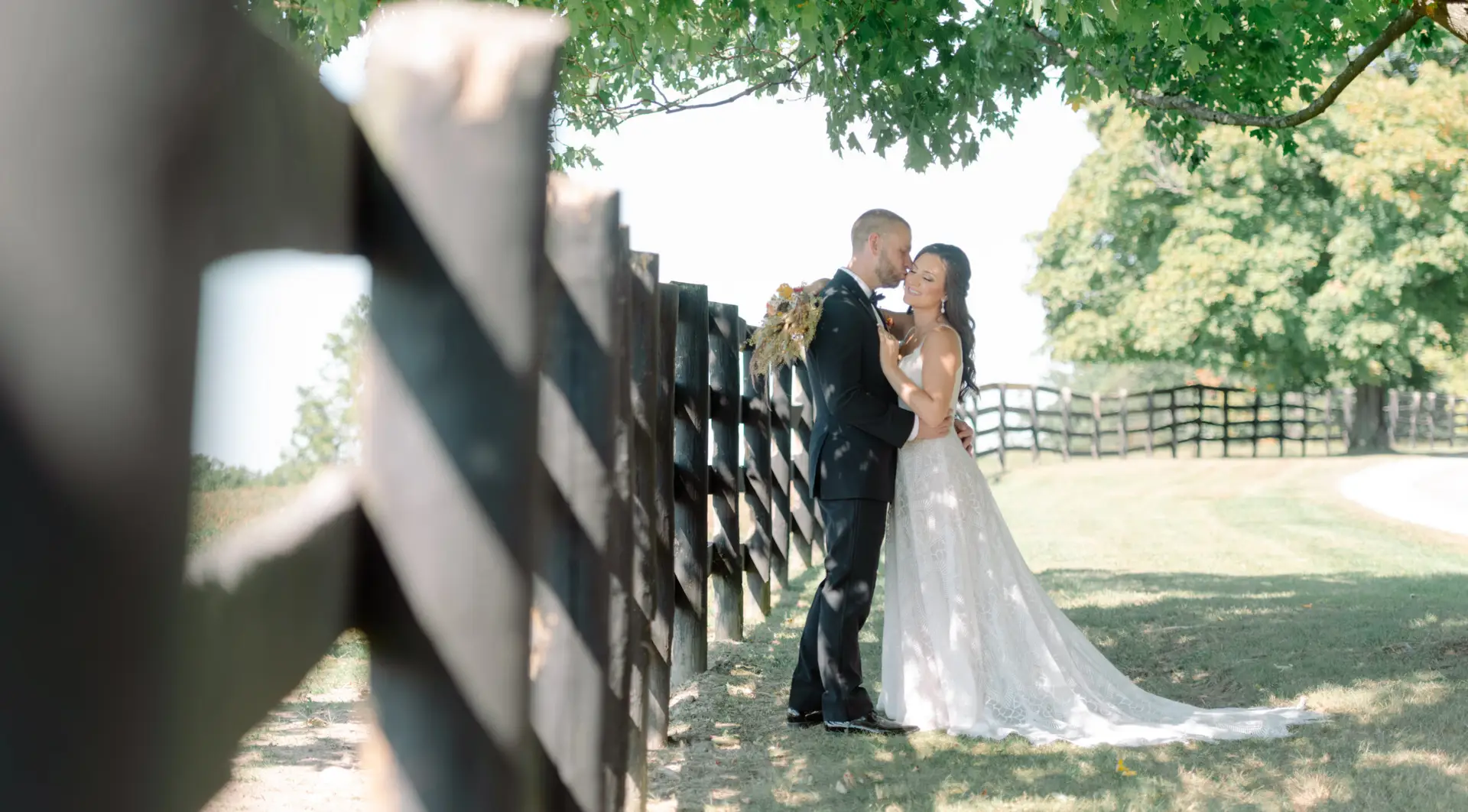 Bride and groom embracing by wooden fence at The Hill Hudson NY outdoor wedding venue with natural light and greenery