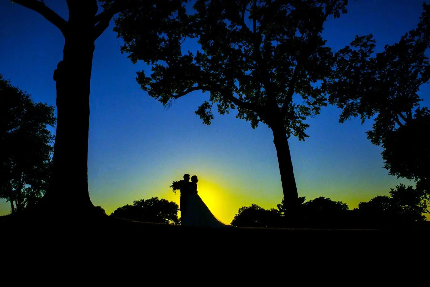 Silhouette of newlyweds at sunset beneath trees at the Village Club of Sands Point in Sands Point, NY.