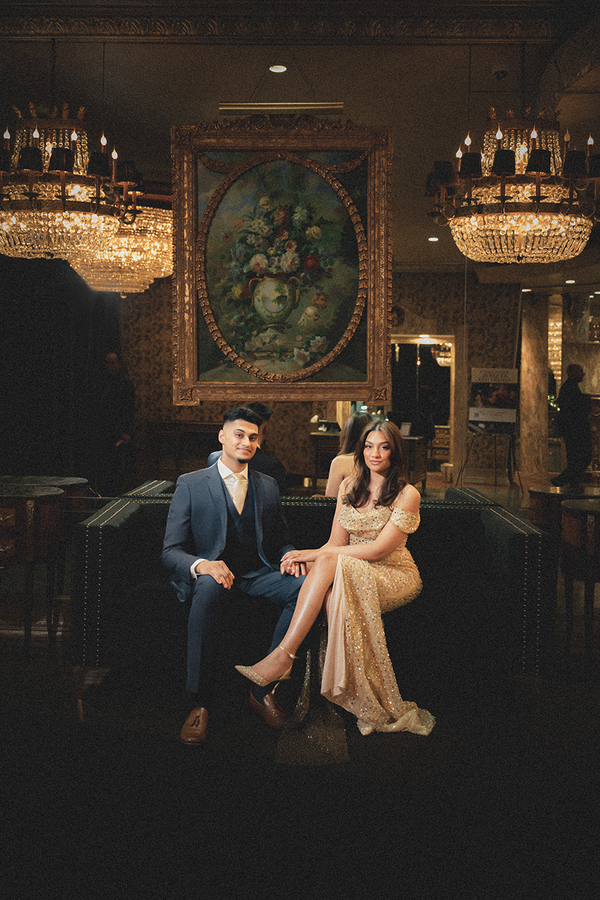 Luxury engagement party portrait at Leonard's Palazzo Great Neck - couple seated under crystal chandeliers with gold sequin gown and navy suit - Long Island engagement photographer JS Visions