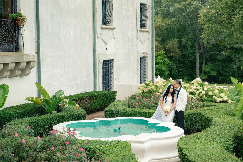 Bride and groom standing beside a fountain in the formal gardens at Vanderbilt Museum in Centerport NY during an elegant wedding portrait session