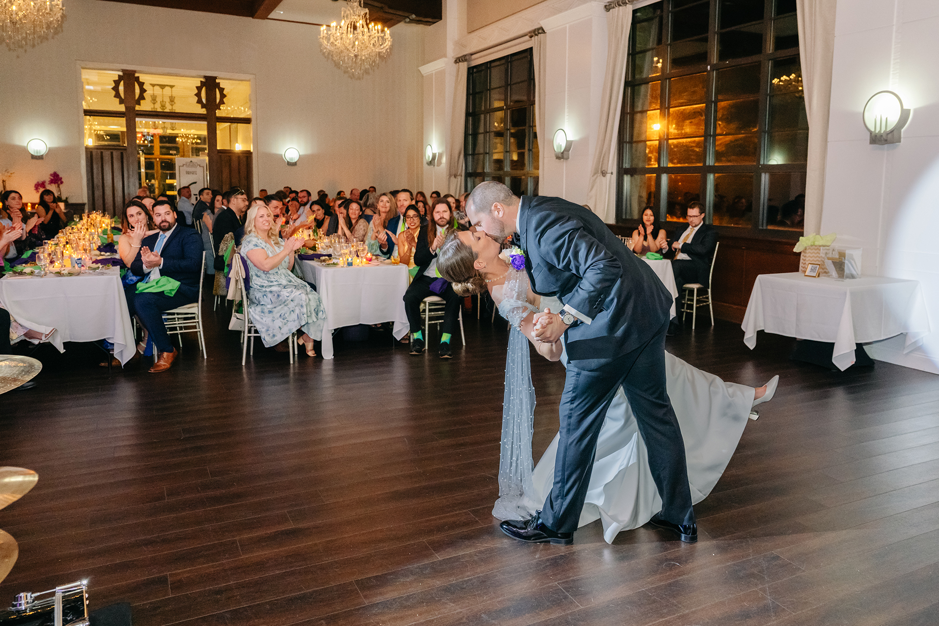 Bride and groom dipping kiss during first dance at Gatsby on the Ocean wedding reception Long Island with guests applauding