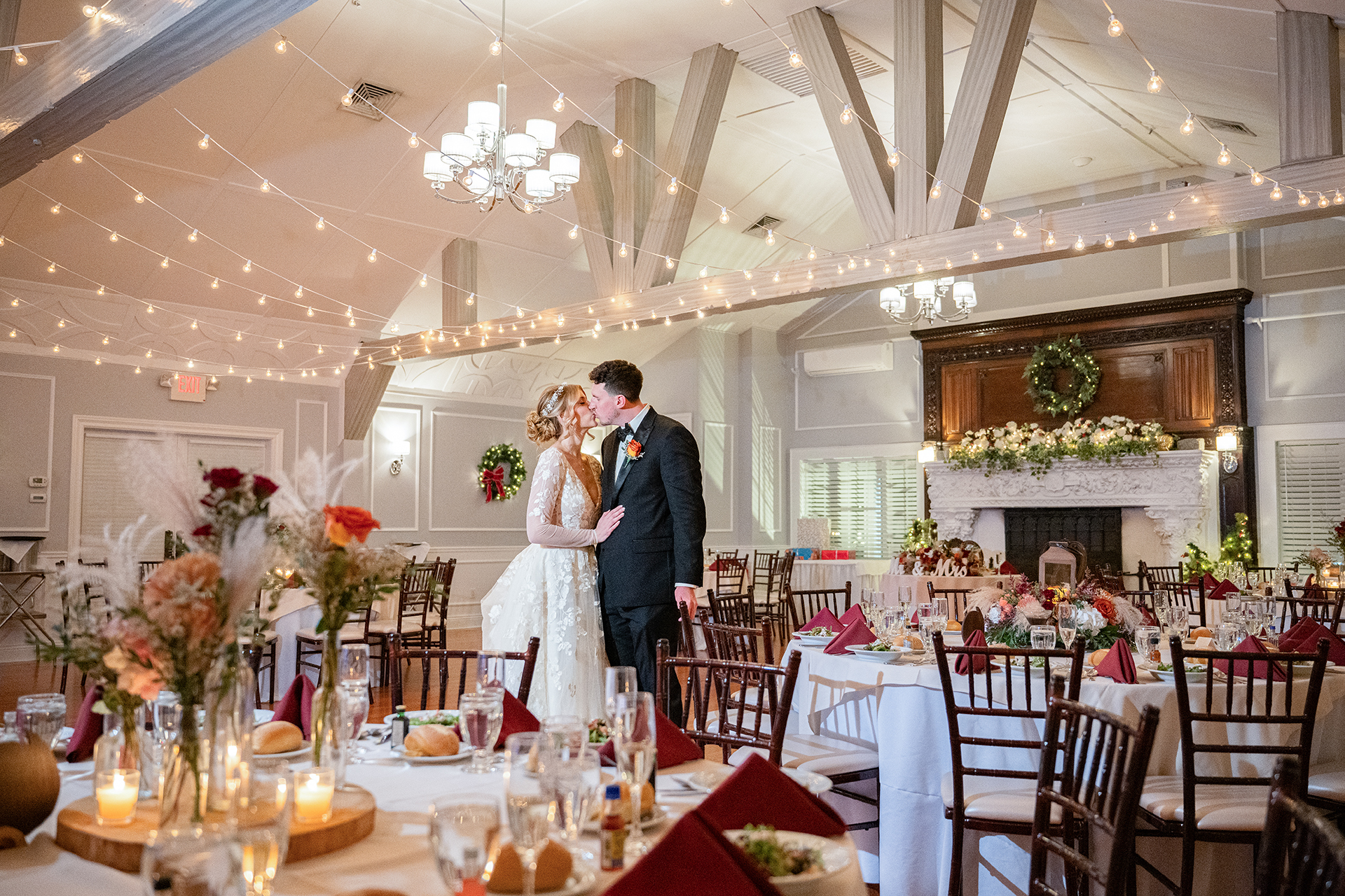 Bride and groom kissing under string lights during elegant indoor wedding reception at Stewart Manor Garden City