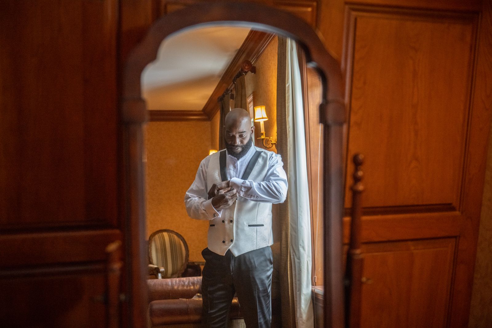 Groom fastening his cufflinks in a mirror while getting ready at The Royalton Mansion