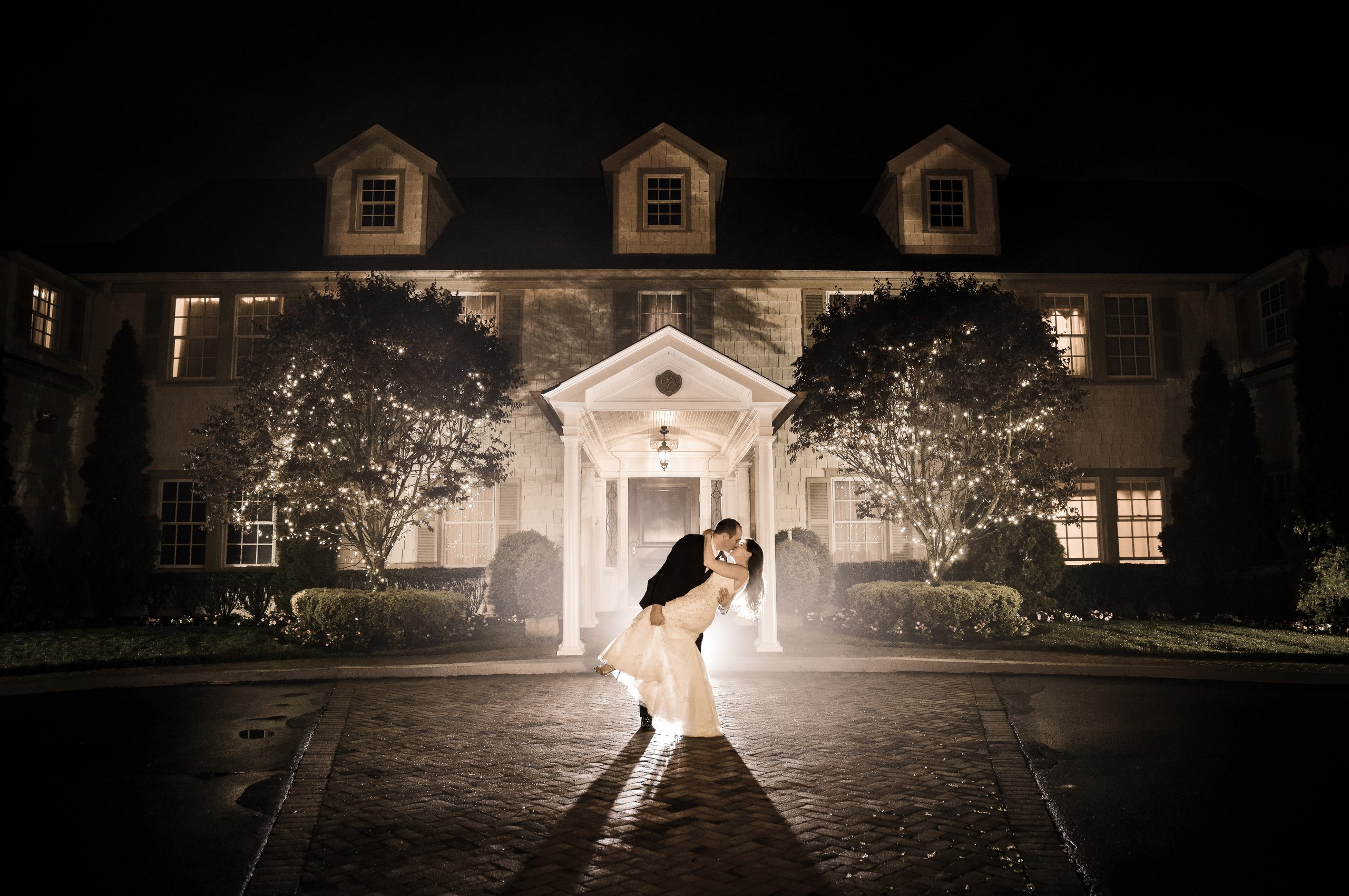 Bride and groom kiss in front of The Royalton Mansion at night, Roslyn Heights NY