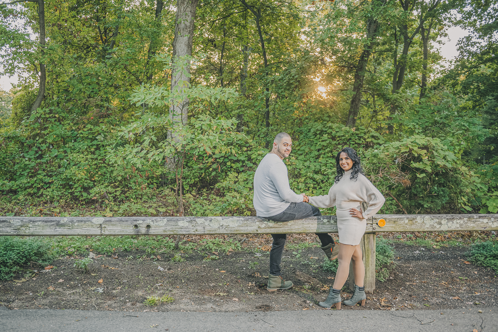 Romantic engagement photo in Hudson Valley featuring couple holding hands by wooden fence surrounded by lush greenery and trees
