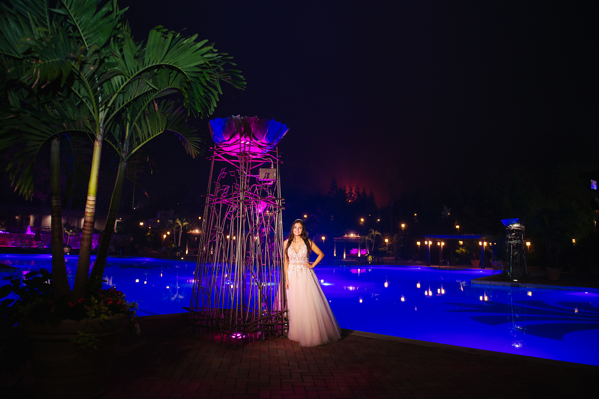 Quinceañera posando junto a la piscina iluminada durante una sesión de retratos nocturna en Crest Hollow Country Club en Woodbury, NY.