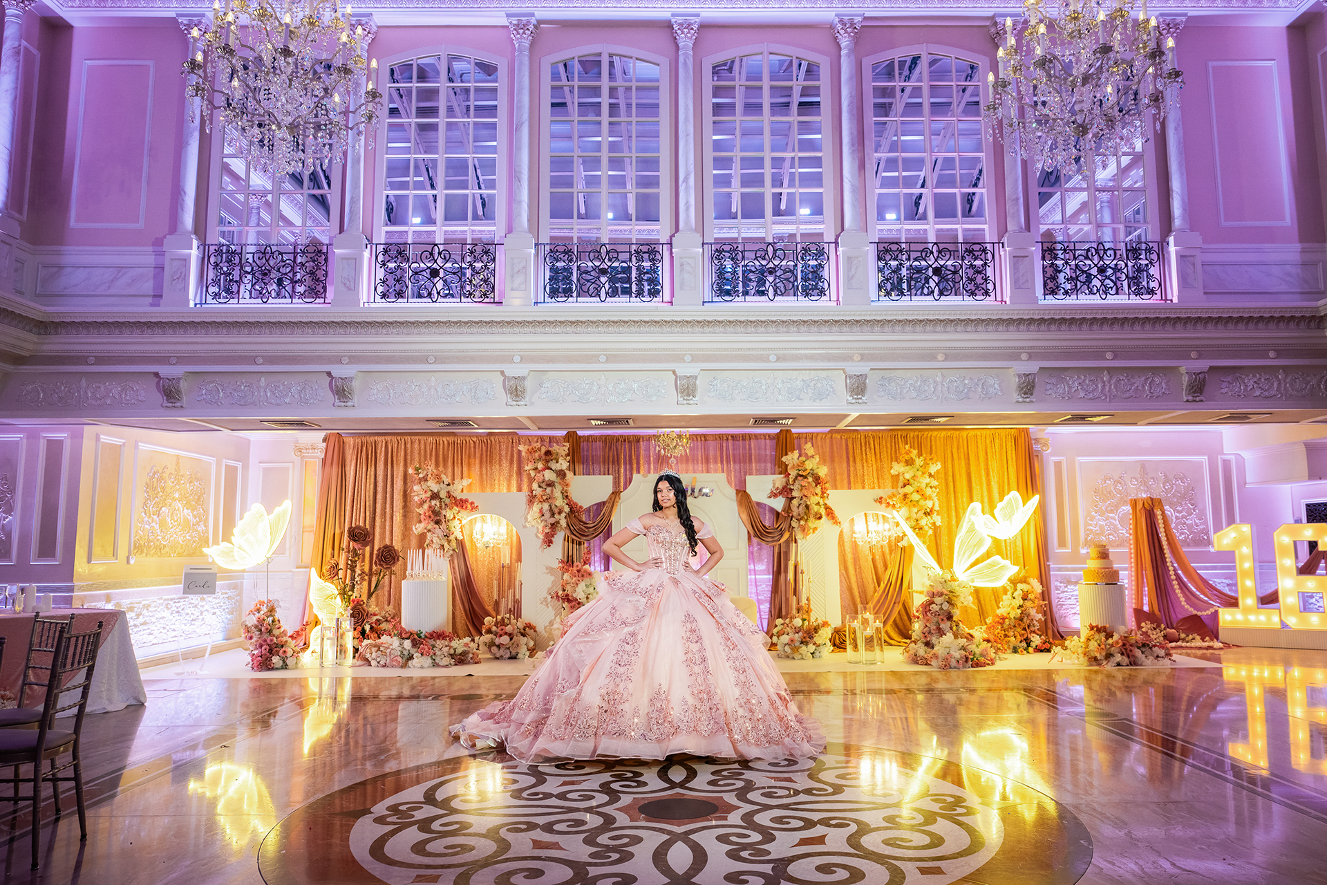Quinceañera posing in the center of a beautifully decorated ballroom before the reception begins.