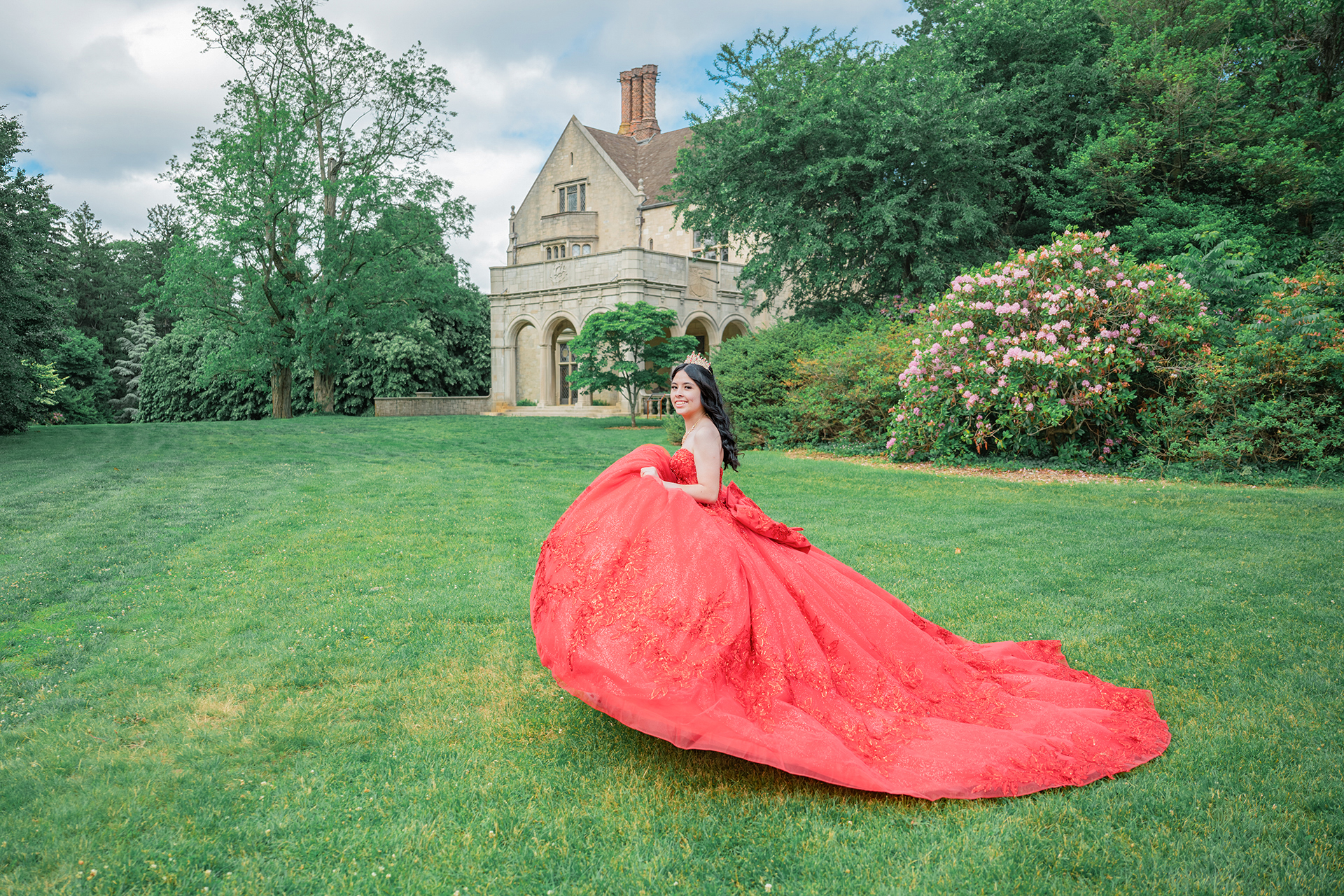 Quinceañera con un vestido rojo de gala posando en el jardín de Planting Fields Arboretum en Oyster Bay, NY.