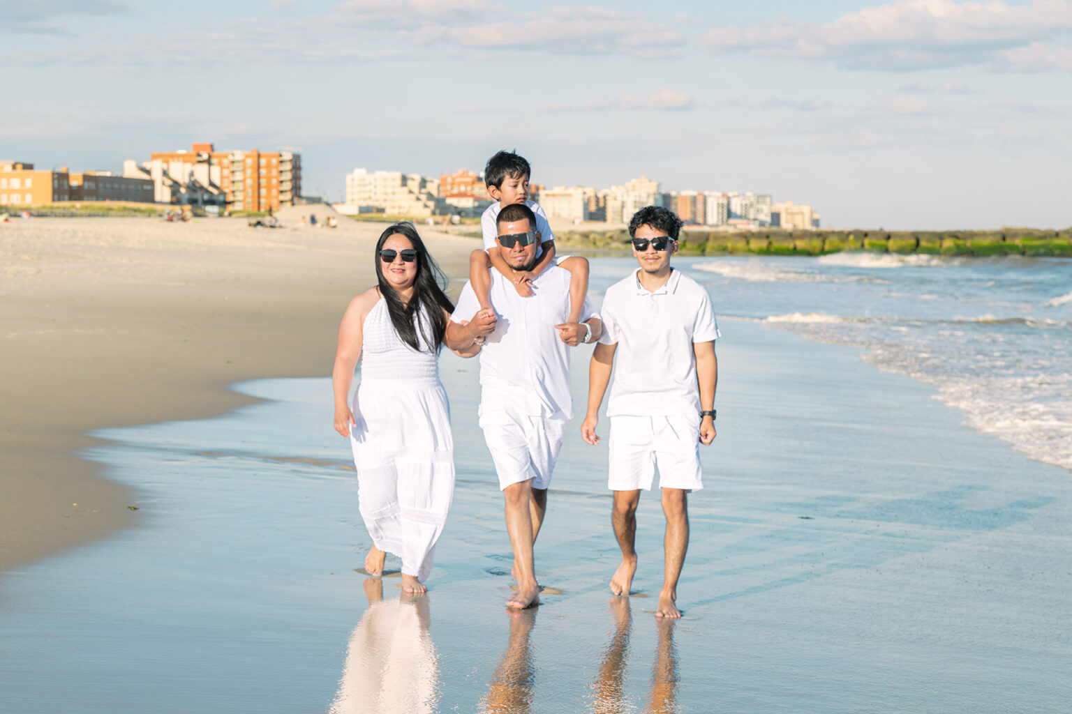 Family of four walking barefoot along the shoreline during a Long Island beach portrait session.