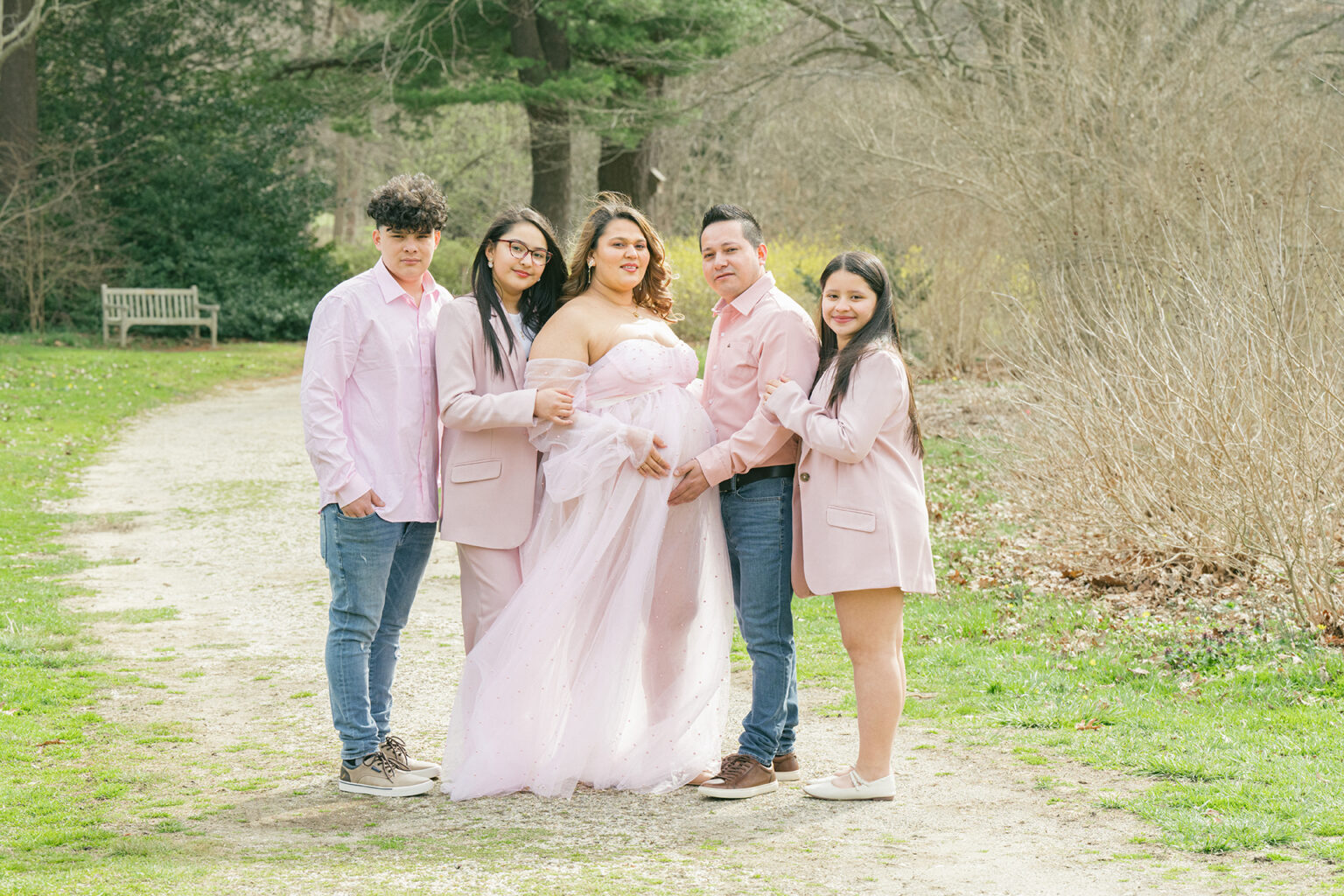 Expectant mother posing with her partner and three children in coordinated pink clothing outdoors.