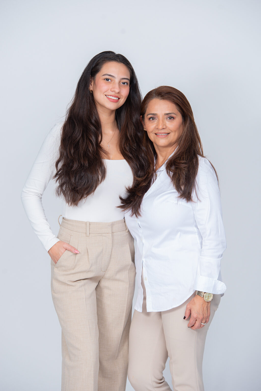 Mother and adult daughter standing together in coordinated white and beige outfits during a Long Island studio portrait session.