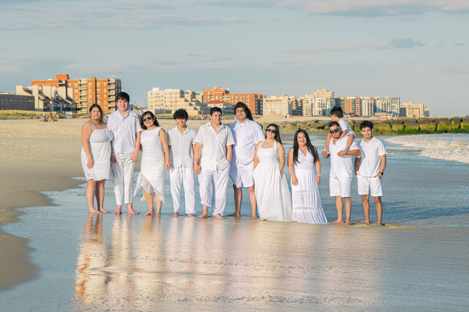 Extended family dressed in white standing together in the surf during a Long Island beach portrait session.