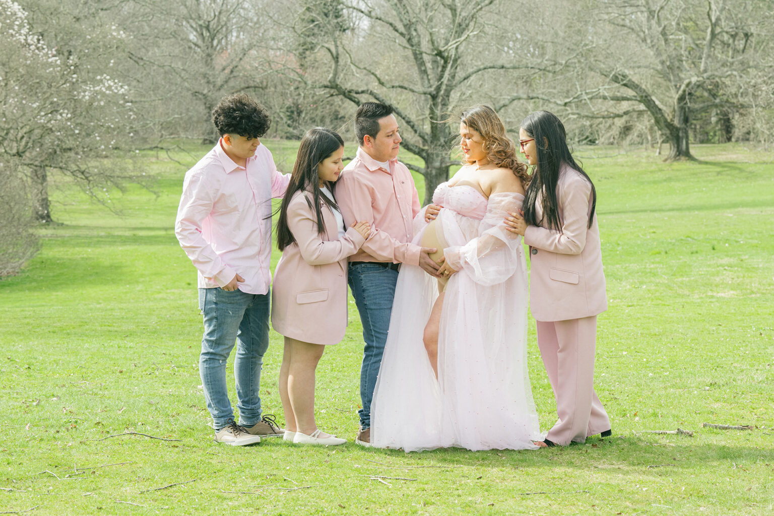 Expectant mother surrounded by her partner and children during an outdoor maternity session in a park.