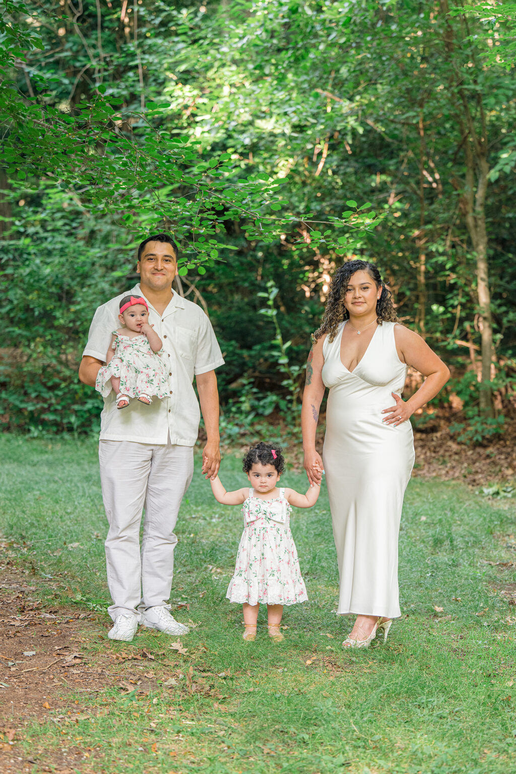 Parents standing with their toddler while holding their baby during a wooded family portrait session.