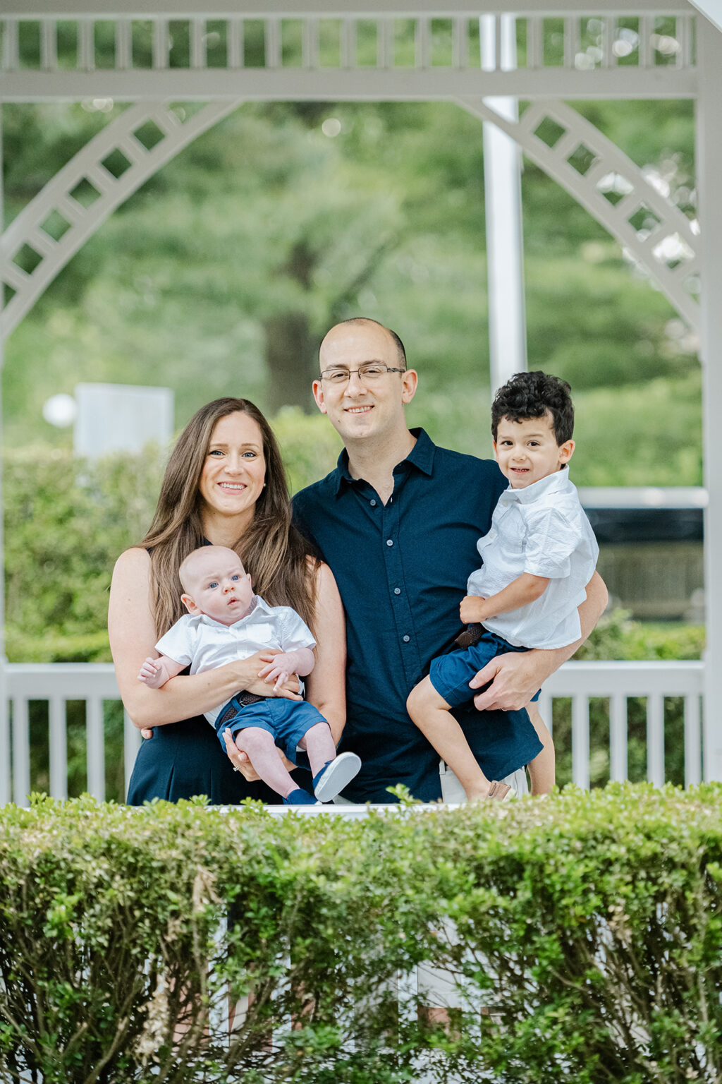 Family of four posing beneath a white garden gazebo during an outdoor portrait session.