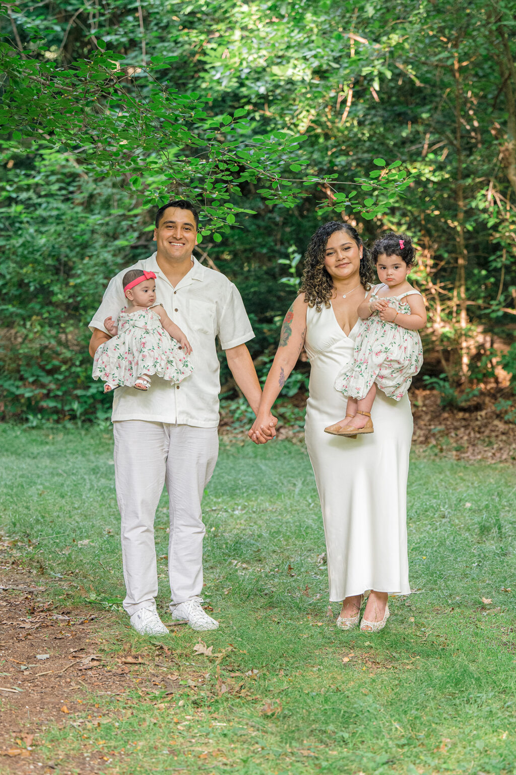 Parents holding their two daughters during an outdoor family portrait surrounded by trees and greenery.
