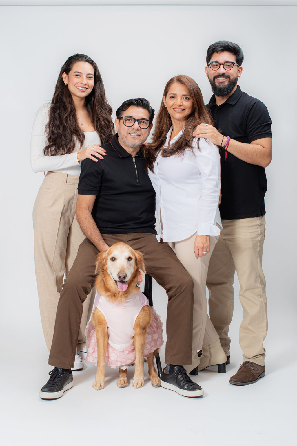 Family of four posing with their golden retriever in a pink outfit during a Long Island studio portrait session.