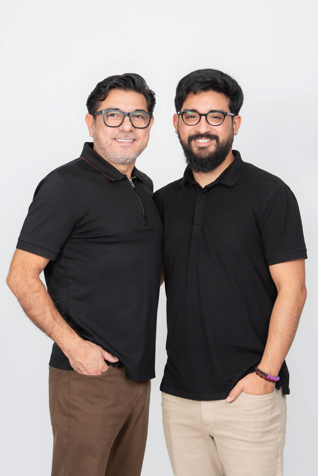 Father and adult son smiling together in matching black shirts during a professional Long Island studio portrait.