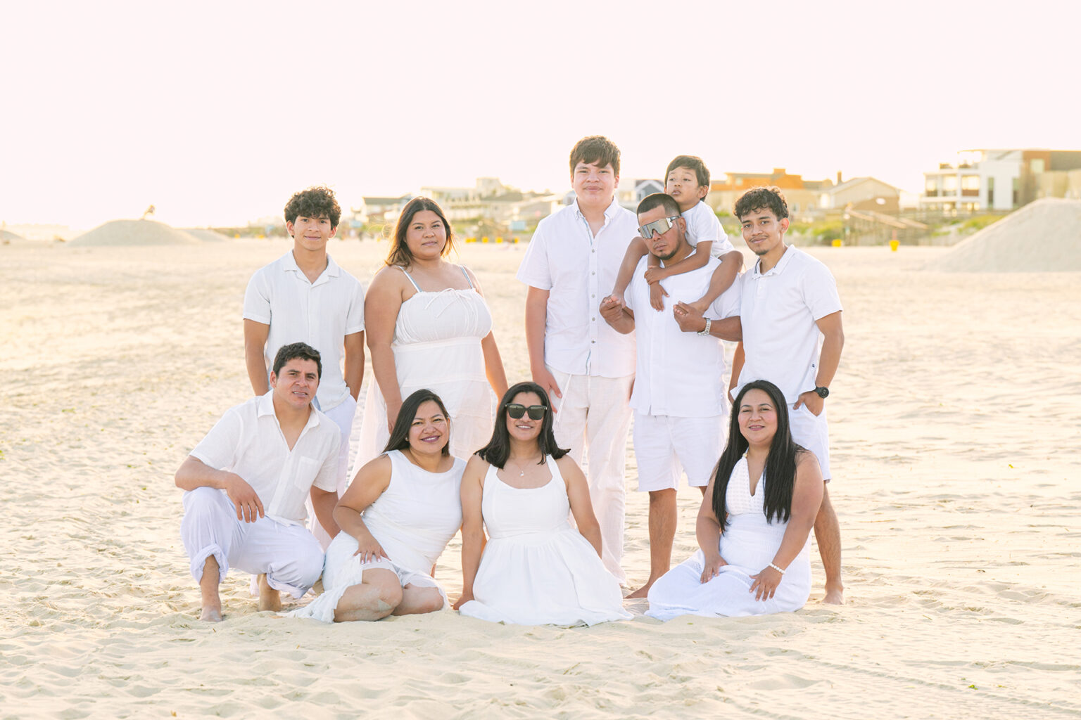 Large multigenerational family dressed in white posing together on the sand during a sunset beach portrait session.