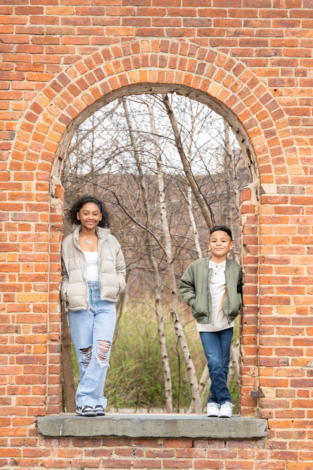 Brother and sister standing inside a historic brick arch during an outdoor Brooklyn portrait session.