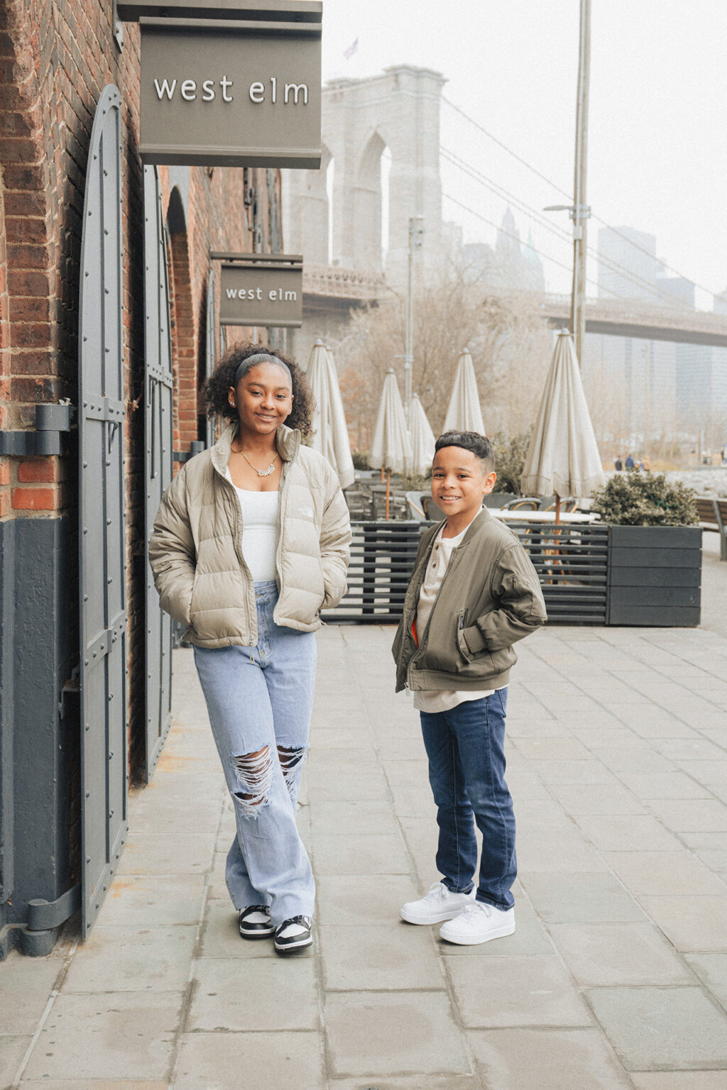 Brother and sister posing near brick buildings with the Brooklyn Bridge visible behind them.